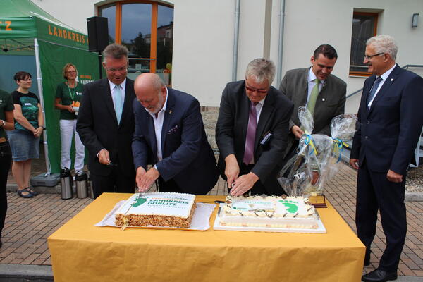 Die Ehrengäste aus Ost und West schneiden die Geburtstagstorte zum 10-jährigen Bestehen des Landkreises Görlitz an. In der Bildmitte (mit lilafarbener Krawatte) Gastgeber Landrat Bernd Lange.
