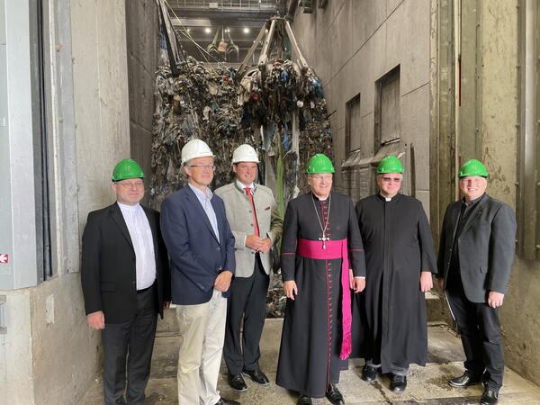 Sechs Männer mit Helmen stehen im Müllkraftwerk vor einer Maschine. In der Mitte steht Bischof  Dr. Rudolf Voderholzer.