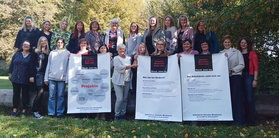 Mehrere Frauen stehen vor Bäumen und halten große Plakate, auf denen Projekte und Handlungsweisen des Arbeitskreises Sexueller Missbrauch vorgestellt werden.