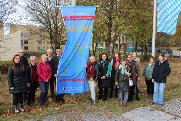 Landrat Ebeling steht mit den Kooperationspartnern des Gedenktags neben einer blauen Fahne mit dem Aufdruck "frei leben - ohne Gewalt"