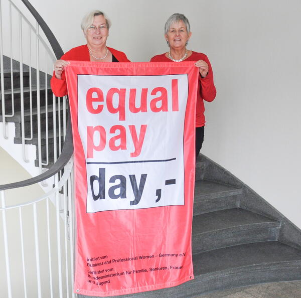 Die beiden Organisatorinnen Helga Forster (Gleichstellungsbeauftragte) und Dorothea Seitz-Dobler (links, Beauftragte für Chancengleichheit am Arbeitsmarkt der Agentur für Arbeit Schwandorf) halten eine Fahne zum Equal Pay Day in den Händen