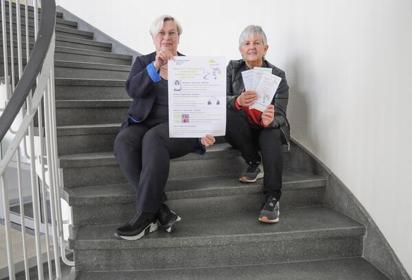 Die beiden Organisatorinnen Helga Forster (rechts) und Dorothea Seitz-Dobler sitzen auf einer Treppenstufe und halten Informationsmaterial in Händen