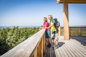 Zwei Menschen stehen auf einem Aussichtsturm und sehen in die Ferne