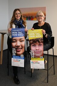 Zwei Frauen halten jeweils ein Plakat in den H&auml;nden