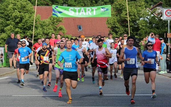 Sportlerinnen und Sportler laufen auf einer Stra&szlig;e. Im Hintergrund steht auf einem Transparent START